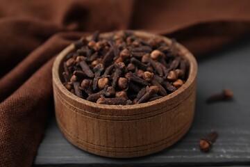 Aromatic cloves in bowl on grey wooden table, closeup