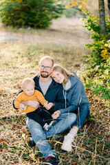 Mom rested her head on the shoulder of dad sitting with his little son on his knees on dry grass