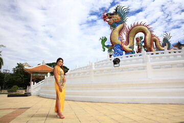 Asian woman wearing a cheongsam poses at shrine with a dragon state on Chinese New Year