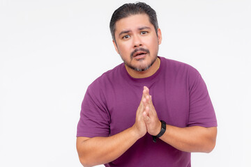 A middle aged man in a purple shirt saying sorry, with hands clasped. Isolated on a white background.