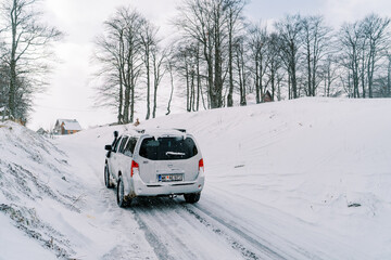 SUV drives along a snowy road in a village. Back view