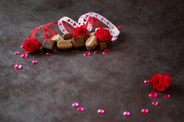 バレンタイン・イメージ　チョコレートと赤いプリザーブドフラワーのバラとハートのリボンとキラキラのデザイン（茶色の背景）