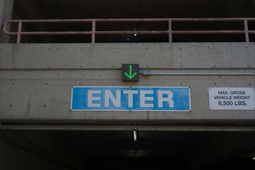 Close up of blue enter sign with green arrow and weight warning sign at a parking garage.