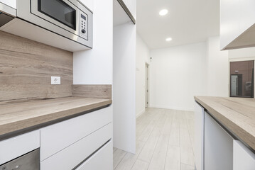 An open kitchen with white cabinets and wood countertops with a matching backsplash and a microwave...