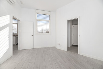 An empty room in a ground floor house with gray parquet floors, white painted walls and access to several rooms