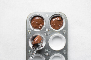 chocolate muffin batter being scooped into a cupcake tin, process of making chocolate muffin