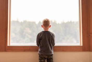 thoughtful child at home looking out his window 