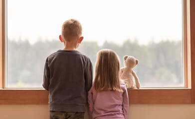 Brother sister at home looking out window  - Powered by Adobe