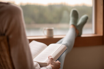 Person relaxing at home reading book feeling relaxed on a cozy winter morning enjoying cup of hot...