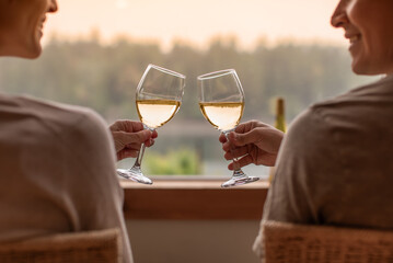 Happy man and woman enjoying glass of wine at home with beautiful nature lake sunset view 