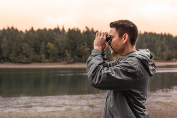 Male hiker looking through binoculars exploring nature wilderness 