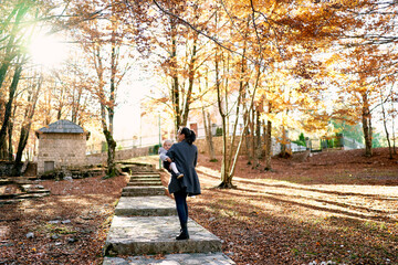 Fototapeta na wymiar Mom with a little girl in her arms walks along a paved path with steps in an autumn park