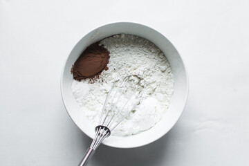 flour and cocoa powder for baking in a white bowl, a ceramic mixing bowl with flour and cocoa powder in it, process of making chocolate cake