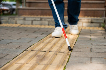 A blind woman walks outdoors using a cane along a tactile yellow tile.