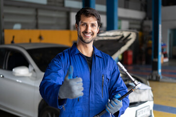 happy latin auto mechanic man checking car with clipboard gesturing show thumbs up and looking at camera in garage cars service . hispanic technician repairing vehicle at garage .