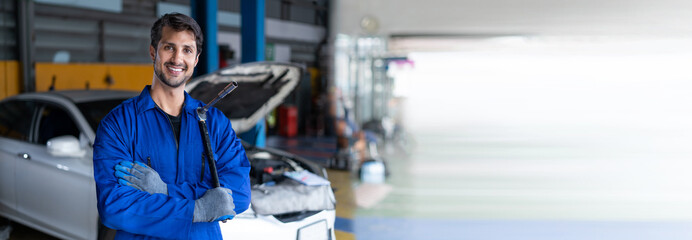 Portrait of latin auto mechanic man holding wrench standing in garage cars service . hispanic technician repairing vehicle at garage . maintenance car repair service . banner and copy space