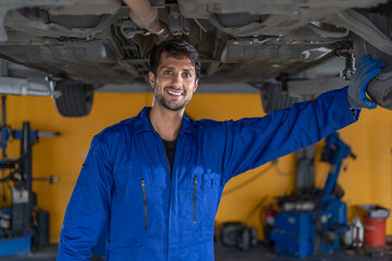 happy latin auto mechanic man checking tires , brakes under car  in garage cars service . hispanic...