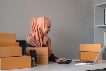 Asian Muslim businesswoman checks stock orders and saves them on her home office laptop. small...