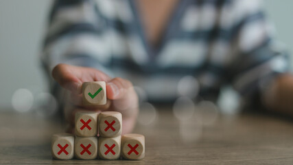 Hand putting wooden cube with tick checkmark right icon over the cross wrong icons. Finding the...