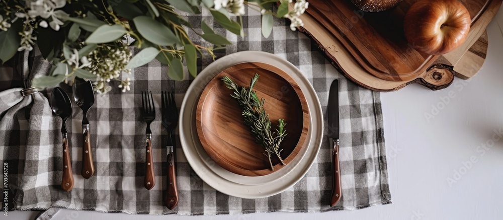 Poster Top-down view of a white table with a grey gingham tablecloth, a round wooden plate, and cutlery.