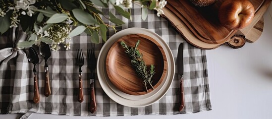 Top-down view of a white table with a grey gingham tablecloth, a round wooden plate, and cutlery.
