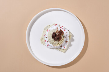 Close-up of an ice cream decorated with waffle crumbs on a white ceramic plate on a pastel background. Eye-catching scene for culinary advertising.