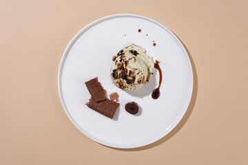 Chocolate is decorated on a dollop of vanilla ice cream on a white ceramic plate on a pastel background. Empty space for design and decoration.