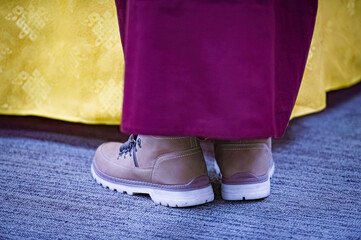 Photo of a Tibetan monk wearing work boots as he leans over a table draped with decorative yellow...