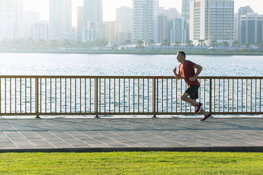 man 50s in sport clothes warm up training run on promenade seafront.
