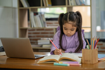 Young Asian girl doing homework online using laptop computer to improve her learning skills.