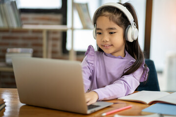 Young Asian female student wearing headphones studying watching video conference, laptop computer,...