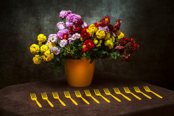 Still life with a bouquet of chrysanthemums in a yellow vase and yellow forks