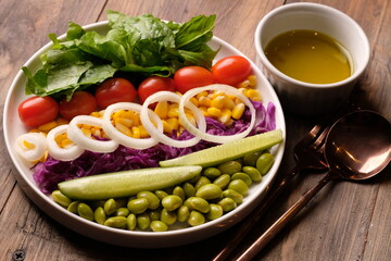 fresh vegetable salad, edamame, sweetcorn, cherry tomatoes, romaine lettuce, sliced cucumber, sliced onions, and purple cabbage. extra virgin olive oil. served on a white ceramic plate. appetizer. 