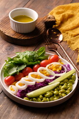 fresh vegetable salad, edamame, sweetcorn, cherry tomatoes, romaine lettuce, sliced cucumber, sliced onions, and purple cabbage. extra virgin olive oil. served on a white ceramic plate. appetizer. 
