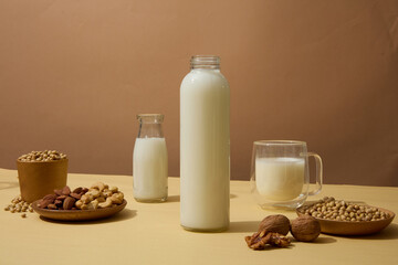 Two unbranded bottle and a glass of organic soy milk. Dishes of walnuts, almond and soybeans...