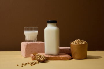 Fototapeta na wymiar Empty label bottle and glass of soy milk displayed on stones. Wooden spoon and bowl of soybeans featured. Soy extract has been shown to stimulate collagen production in the skin