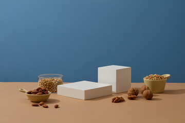 White podiums in cube and square shaped are arranged on beige surface with types of nuts. Concept...