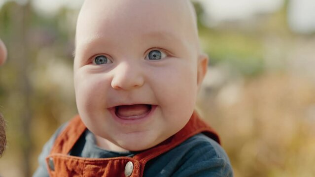 Portrait of cute infant baby on parent hands outdoors. Adorable little child smile. Dad play with kid while walking. Close Up on joyful baby face