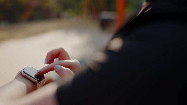 Woman athlete looking at smartwatch and check heart rate during cardio workout outdoors. Young female using smart watch for track fitness progress. Healthy lifestyle concept