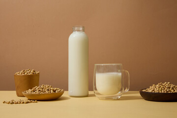 Front view of wooden dishes and bowl of soybeans displayed with bottle and glass of soy milk. Beige...