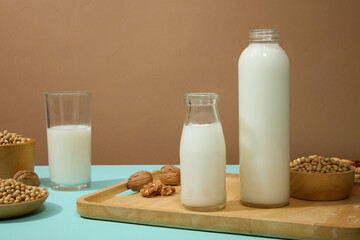 Organic product advertising with bowls of soybeans, walnuts and bottles of milk arranged over brown background. Blank label bottle for mockup
