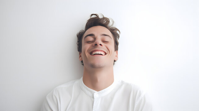 a happy young man with eyes closed smiling lying on white surface, isolated on white background.