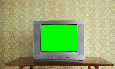 An old TV with a green screen on the nightstand against the background of wallpaper.