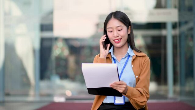 Confident Asian woman with a smile standing holding notepad and tablet at out side office. big city