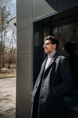 The image depicts a man wearing glasses and a suit, smiling, and standing