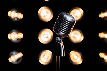Fototapeta na wymiar Retro metal microphone on stand, placed on dark stage during event in studio. Close up of silver mic with blurred bulb lights on background, with copy space. Concept of event, sound, music.