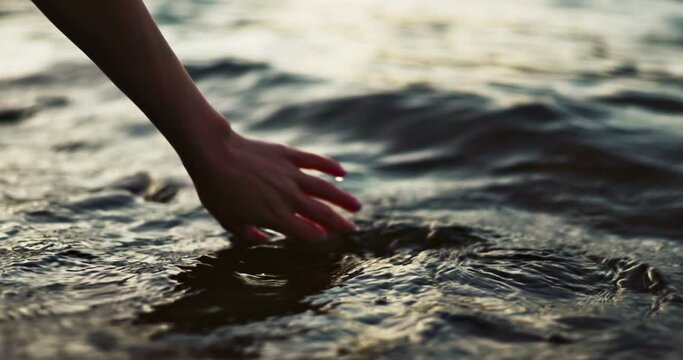 Closeup, hand and water in morning by sea with touch, waves and nature on vacation in sunshine. Person, fingers and outdoor vacation by river, lake and ocean in environment with ripple in Japan