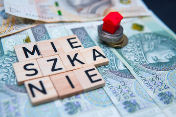 The inscription Mieszkanie next to Polish money and a red house. A concept showing the purchase of an apartment. Mortgage loan and real estate market in Poland