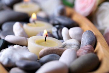 Wooden bowl with spa stones and candles on wooden  table, on flowers background