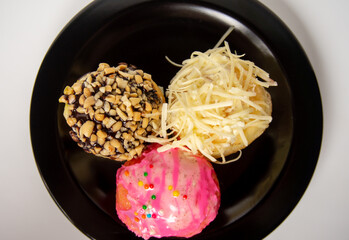 three mini donuts with delicious flavors on a black plate on a white background